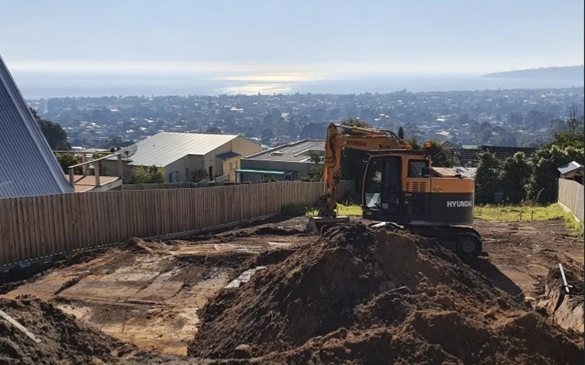 Excavator forming a site cut with spoil heaps, overlooking the bay